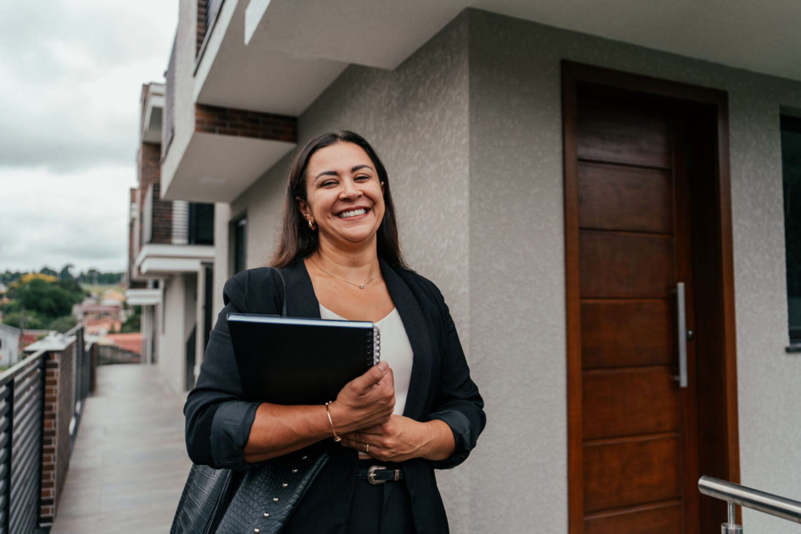 Smiling woman holding notebook outside a building.